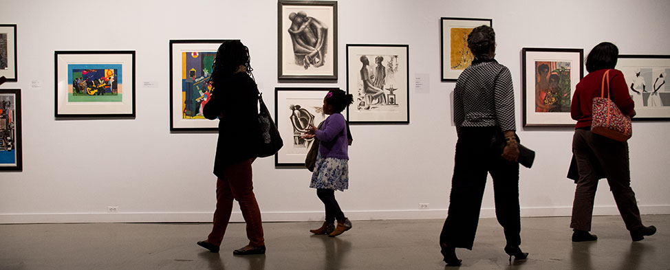 A mother and her daughter examine the exhibit of African American art at the August Wilson center, and two other women walk by in the opposite direction.