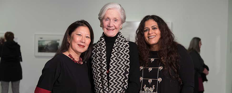 Susan Tsu, Carol Brown and Sarika Goulatia standing together in the gallery at the August Wilson Center. Visitors are milling around in the background.