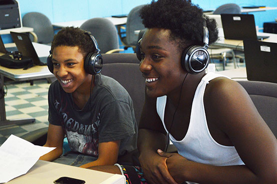 Two young men working on laptops, wearing headphones.