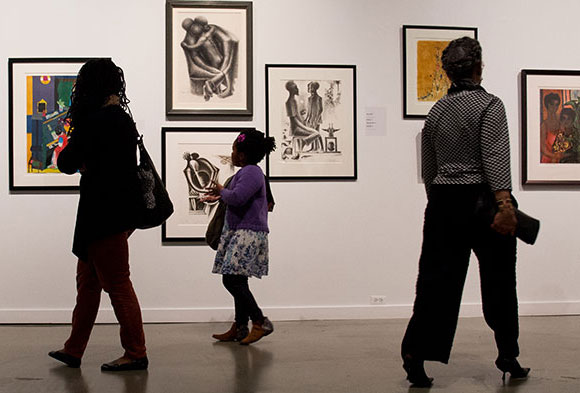 A mother and her daughter examine the exhibit of African American art at the August Wilson center, and two other women walk by in the opposite direction.