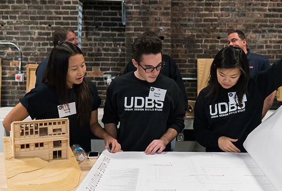 Three students from the Urban Design Build Studio are shown looking through blueprints during the Project RE dedication at Construction Junction.