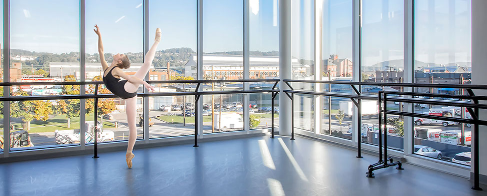 Ballet dancer strikes a pose in the Ryan Studio of the new Byham Center for Dance. A view of the Strip District of Pittsburgh can be seen through the expansive windows in the background.