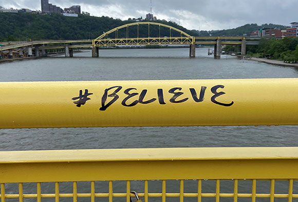 Yellow bridge railing with #believe written in black ink.