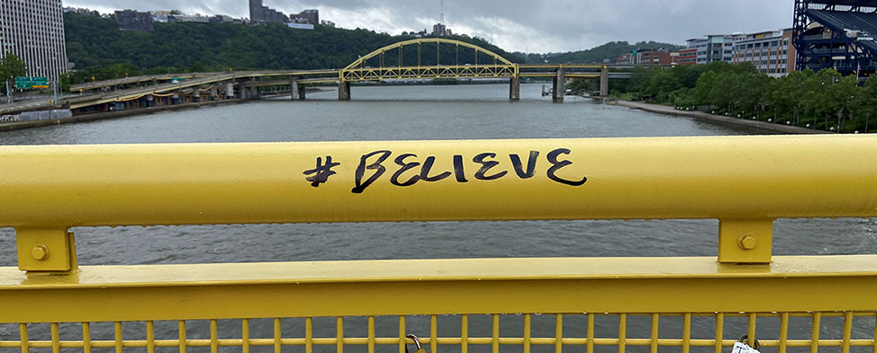 Yellow bridge railing with #believe written in black ink.