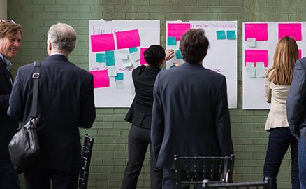 Group of people with their backs to the camera, working together with post-it notes to organize thoughts and ideas at the p4 Pittsburgh conference.