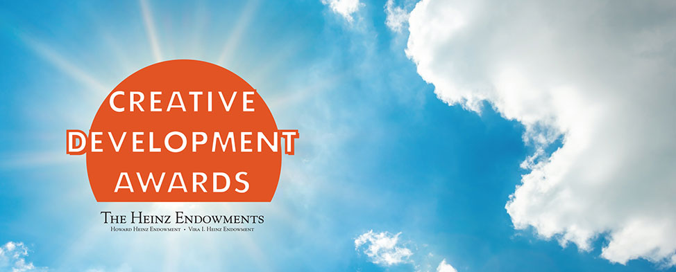 White clouds, blue sky, and in place of the sun - orange circle containing the words, "Creative Development Awards"