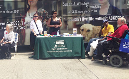 Photo taken during the 3 Rivers Arts Festival celebrating the 25th anniversary of the Americans with Disabilities Act. Image shows several people in wheel chairs around an informational table provided by Achieva.