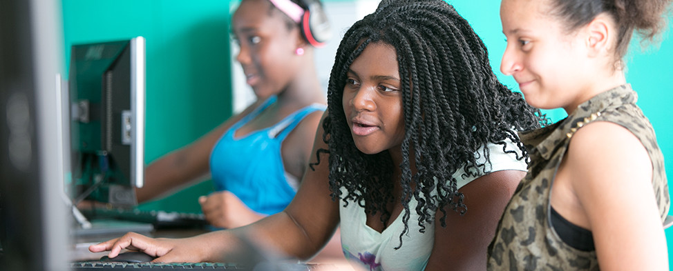 Three participants of the Gwen’s Girls program are sitting in front of computers and interacting with each other as they hone their skills.