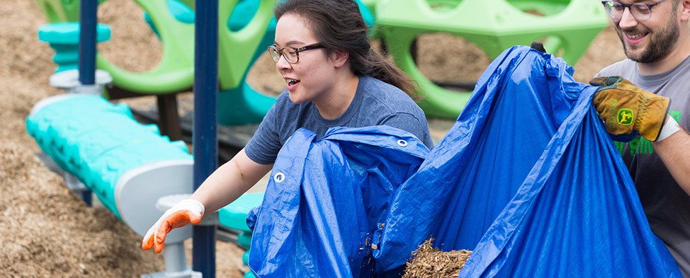 Two volunteers carrying mulch in a blue tarp on Build Day at the Hazelwood KaBOOM! playground.