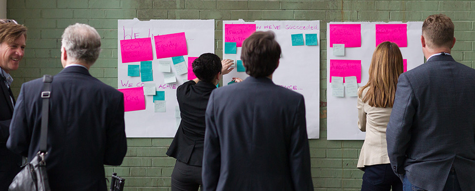 Group of people with their backs to the camera, working together with post-it notes to organize thoughts and ideas at the p4 Pittsburgh conference.