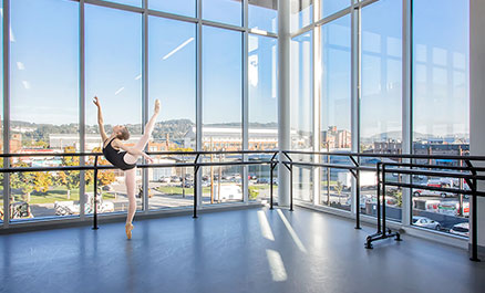 Ballet dancer strikes a pose in the Ryan Studio of the new Byham Center for Dance. A view of the Strip District of Pittsburgh can be seen through the expansive windows in the background.