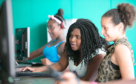 Three participants of the Gwen’s Girls program are sitting in front of computers and interacting with each other as they hone their skills.