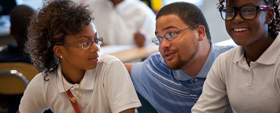 Heinz Fellow, Matthew Tansey, kneels down to assist two female students with their studies at Westinghouse High School, part of the Pittsburgh Public Schools.