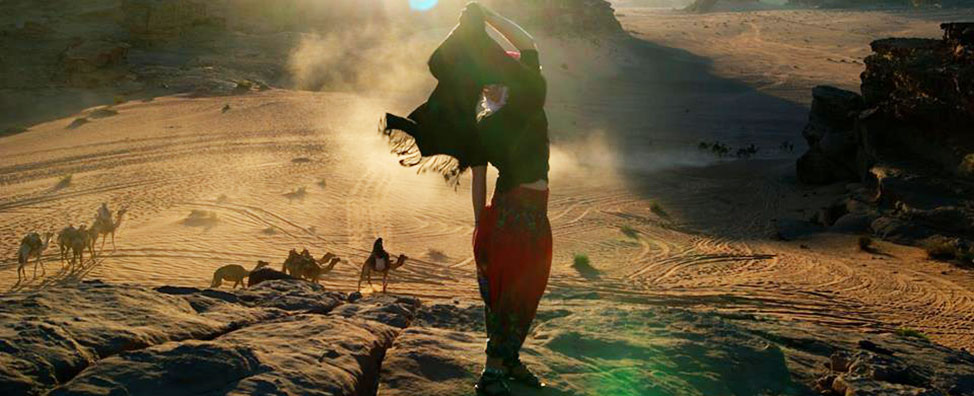 Kimberly Beechan, a Vira I. Heinz Program for Women in Global Leadership participant, standing in the desert in Jordan. She is overlooking a view of the desert, with many camels crossing in front of her and the mountains in the background.