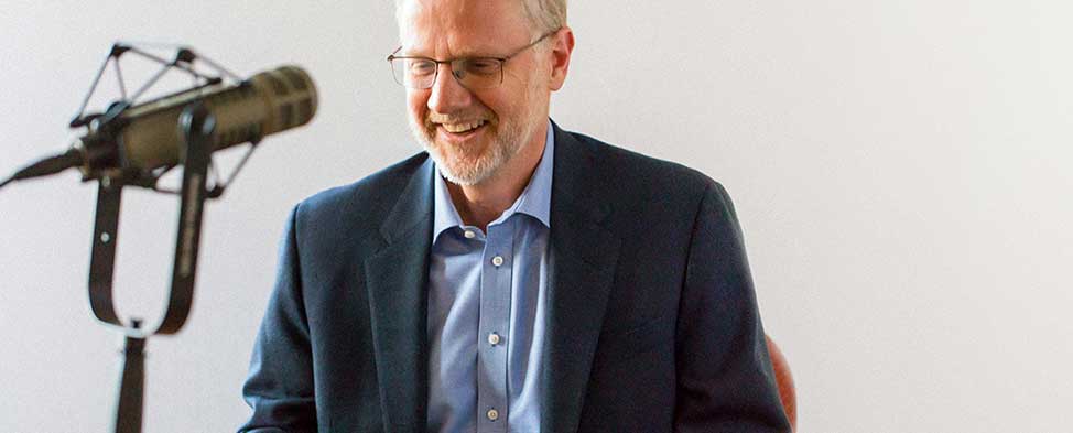 Grant Oliphant smiling in conversation with podcast guest seated behind a microphone.