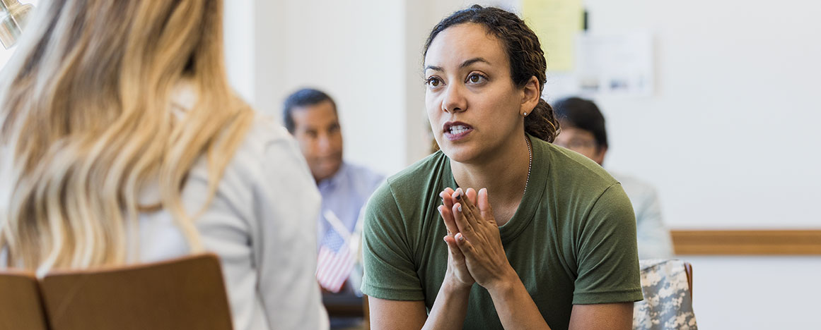 A woman veteran dressed in an Army green t-shirt participating in a group discussion in a supportive group setting.