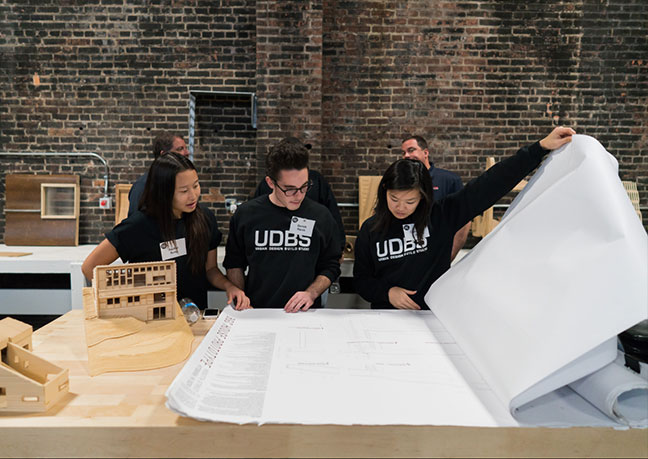 Three students from the Urban Design Build Studio are shown looking through blueprints during the Project RE dedication at Construction Junction.